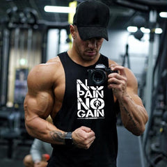 Muscular man holding a camera with 'No Pain No Gain' tank top in a gym setting