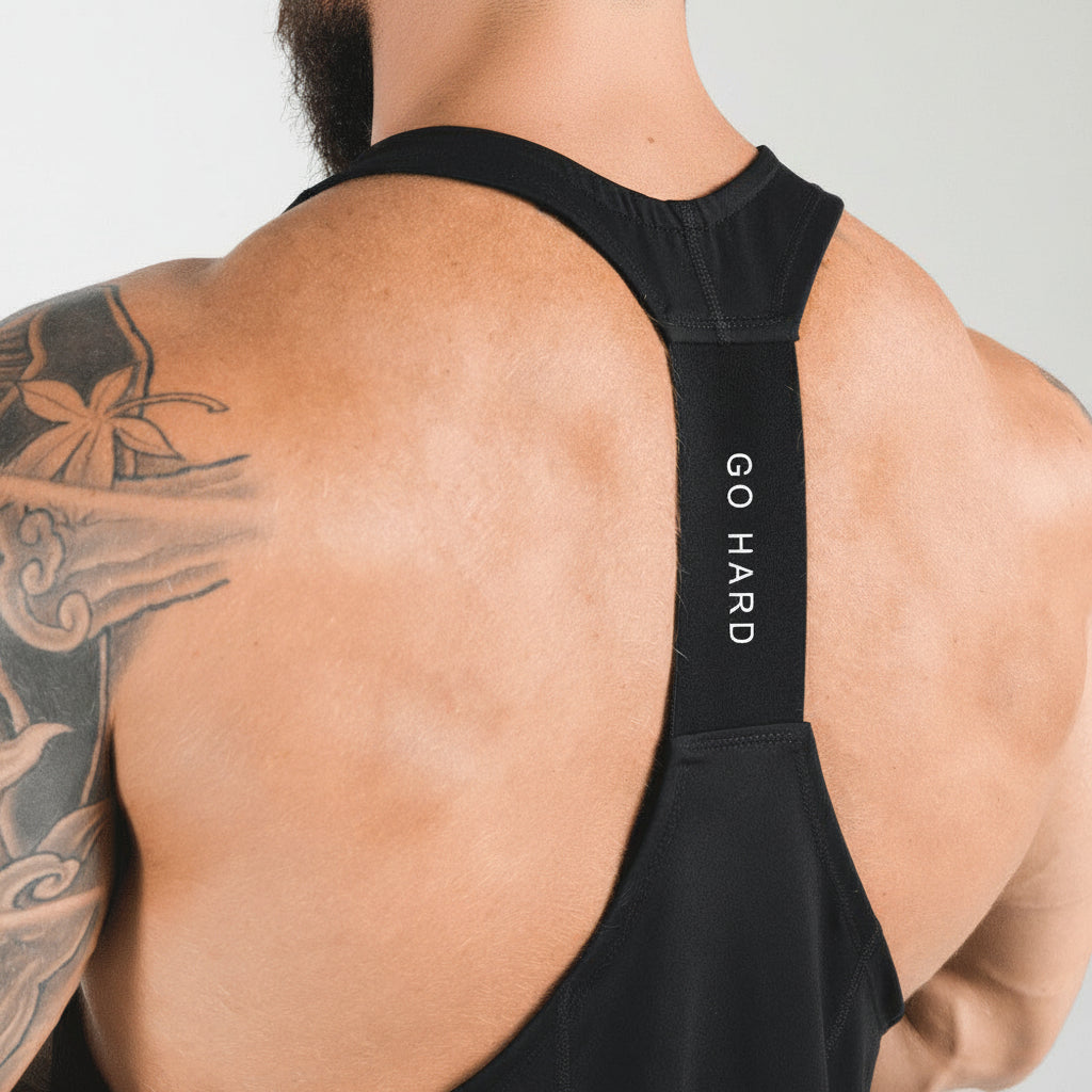 Person wearing a black tank top with 'GO HARD' text on the back, showcasing tattoos.